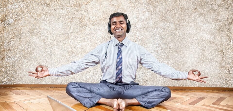 20047808 - indian businessman listening to the music with headphones and doing meditation near the laptop